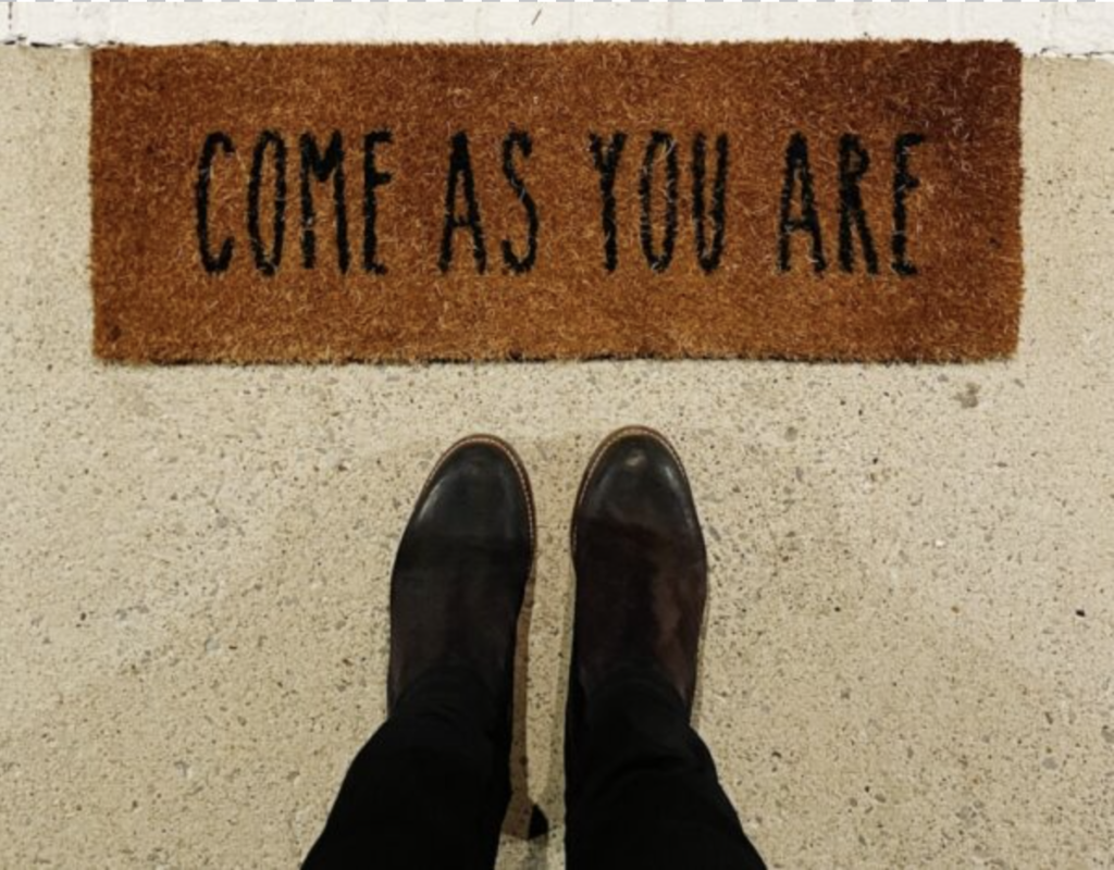 person standing on brown and black welcome floor mat that says Come As You Are